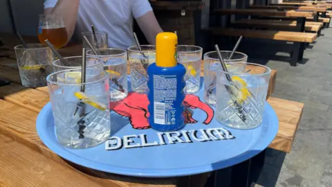 Mark Ansell/BBC A blue tray with suncream and glasses of water on for customers to use. The tray is on a picnic bench in the beer garden of the Head of Steam pub in Sheffield city centre.