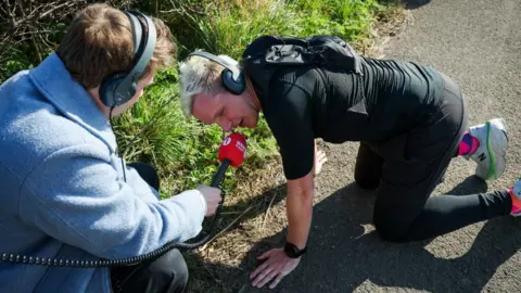 Getty Images Jamie Laing diwawancarai oleh Matt Edmondson pada hari keempat tantangan maratonnya pada 20 Maret 2025 di Kegworth, Inggris. Jamie mengenakan T-shirt dan legging hitam, dan merangkak di tanah berbicara ke dalam mikrofon radio 1 