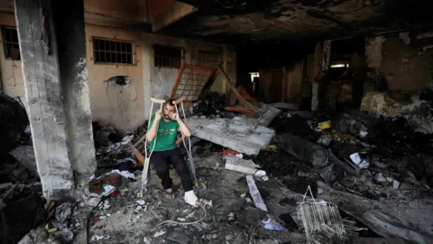 Reuters An injured man sits inside Abdulfattah Hamoud school in Gaza City after it was damaged in an Israeli air strike (25 June 2024)