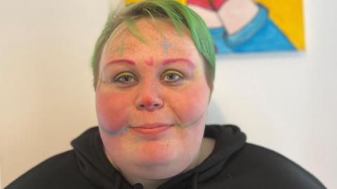 Axel Pritchedd wearing brightly-coloured face paint and a black hoodie