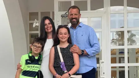 Hannah Quigley-McKie Hannah Quigley-McKie pictured with her partner and two children in front of a doorway. 