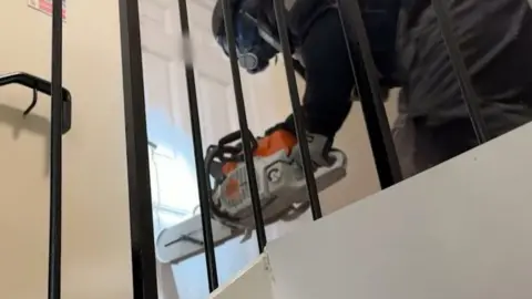 A man is holding a chainsaw and sawing it through a white door.