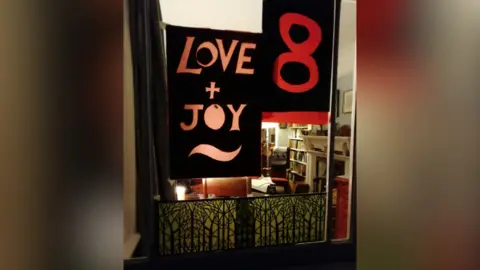 Anna Eden A house window with a decoration of a the words "Love + Joy" on display. The number 8 is displayed beside it.