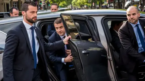 Getty Images Bodyguards protect Mr Macron as he exits a car, May 2017