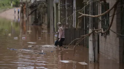 Getty Images A woman wades through the water as the flood starts receding in Brazilian municipality of Raposos