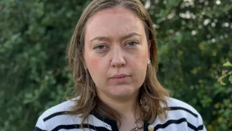 A woman with brown shoulder-length hair and a stripey top 
