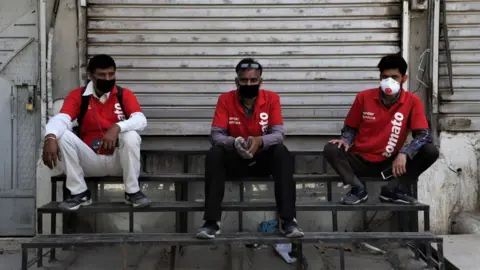 Getty Images Zomato Food Delivery boys wearing protective masks sit near closed shutters amid Covid-19 (Coronavirus) lock down in Gurugram on the Outskirts of New Delhi, India on 07 April 2020.