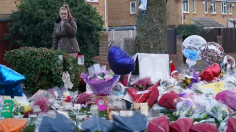 PA Media A woman lays flowers among the tribute left near the park in Kingshurst