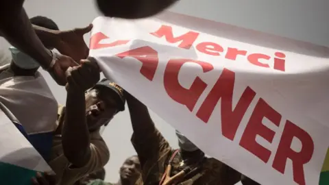 AFP Protesters holds a banner reading "Thank you Wagner", the name of the Russian private security firm present in Mali, during a demonstration organised by the pan-Africanst platform Yerewolo to celebrate France's announcement to withdraw French troops from Mali, in Bamako, on February 19, 2022.