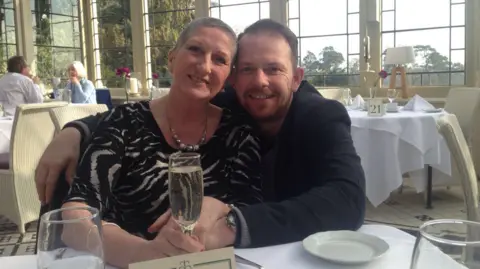 Linda Morris pictured next to her son Craig. She's holding a glass and smiling at the camera.