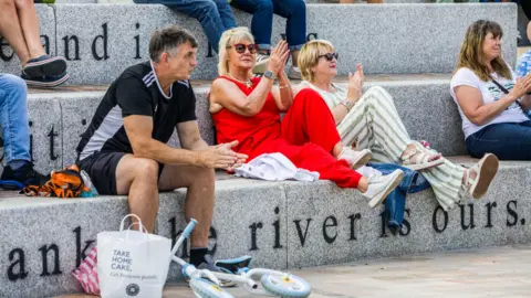 Stockton Council Three women and a man clap while they watch a performance at the waterfront's amphitheatre.