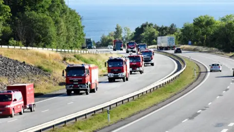 Reuters A convoy of Polish Fire Brigade passes lake Vattern on their way to Uppsala, after a rest and refuelling in Uppsala the Polish firefighters will continue during Sunday to central Sweden where they will help to put out the major wild fires