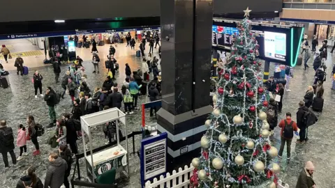 BBC Passengers waiting at Euston Station with a Christmas tree in the foreground