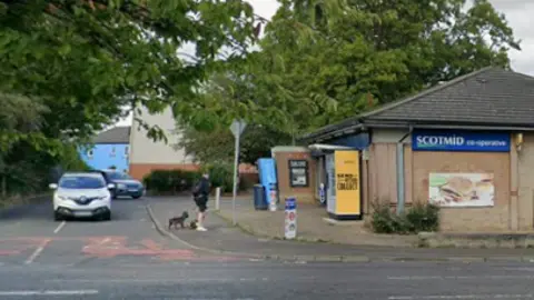 A street view of a shop on a residential street with trees behind