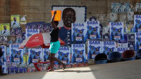 Reuters A woman walks past blue posters of the Odinga, who is running to be president. The poster has a picture of him and the word, Baba is written in Nairobi - Monday 25 July 2022