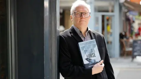 Getty Images Journalist and author Stephen Davis poses with his new book Operation Trojan Horse