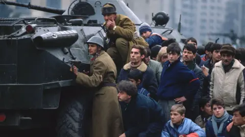 Getty Images Romanian soldiers and civilians take cover behind a tank in Bucharest's Palace Square in December 1989