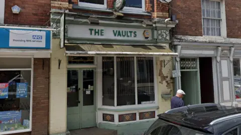 A small pub called "The Vaults" is pictured which has light green doors and a light green and white sign.