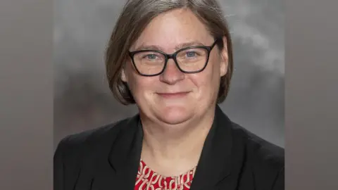 Dundee University Angela Scott, a woman with glasses and short grey hair, smiles wearing a dark blazer and patterned top