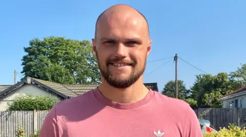 James Russell wear pink T-Shirt and is smiling. He has a beard and is looking at the camera. 