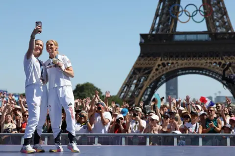 Getty Images Equestrian eventing team gold medallists Ros Canter and Laura Collett pose for a photo at the Olympic Games in Paris in 2024. There are crowds of people in the background, standing in the shadow of the Eiffel Tower.