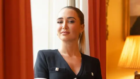 Georgia Harrison pictured in front of orange curtains, wearing a black top