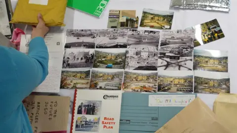 Calderdale Council A table covered in documents and A5 photographs. A blue folder in the bottom right reads 'Our 1998 Thoughts'.