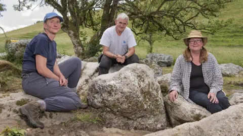 Historic England Archive two men and a woman sat by a boulder in the countryside