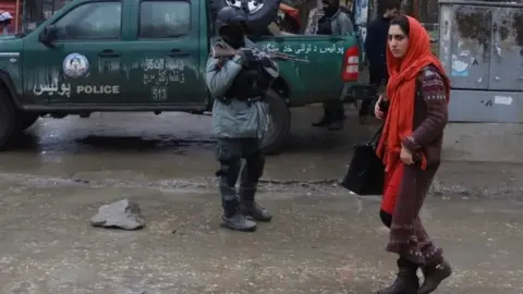 EPA An Afghan woman walks near a security officer in Kabul