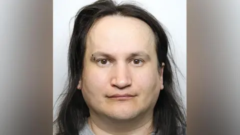 Greater Manchester Police Custody image of Marcin Majerkiewicz with a brow piercing, long dark brown hair and wearing a grey t-shirt.