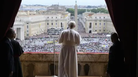 EPA Pope Leo in white, seen from behind, addressing a large crowd gathered in the square below