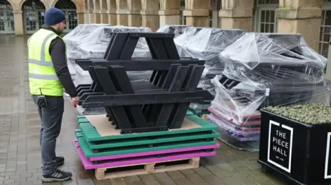 British Recycled Plastics A man in a yellow hi-vis stands next to some stacked picnic benches made from recycled plastic at The Piece Hall in Halifax 