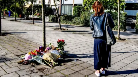 Getty Images A woman walks by flowers laid outside the home of the murdered lawyer Derk Wiersum, on September 19, 2019