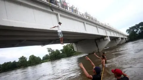 Reuters A Honduran migrant, part of a caravan trying to reach the US jumps from the bridge that connects Mexico and Guatemala to avoid the border checkpoint in Ciudad Hidalgo, Mexico, 19 October 2018