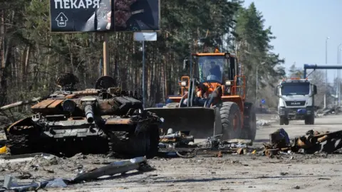 Getty Images The remnants of a Russian tank is cleared away near Kyiv by a digger