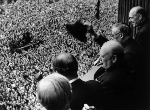 Getty Images Prime Minister Winston Churchill addresses a huge crowd from a balcony in the Ministry of Health building on VE Day, 8 May 1945