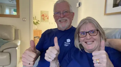 BBC Meg Richards sits alongside husband Peter, sticking their thumbs up and smiling as they wear purple team GB shirts