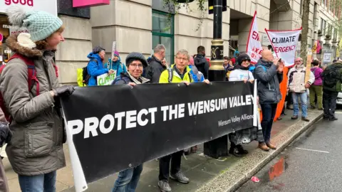 Andrew Sinclair/BBC Protestors holding up sign which reads Protect the Wensum Valley