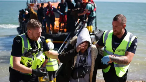 Getty Images An interforce officer and a border force officer help a woman on the beach at Dungeness on the southeast coast of England, on 16 August 2023
