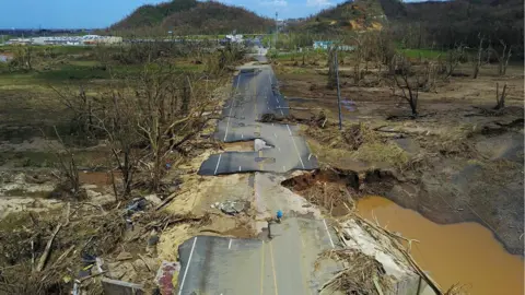 AFP/Getty A man rides his bicycle through a damaged road in Toa Alta, west of San Juan, Puerto Rico