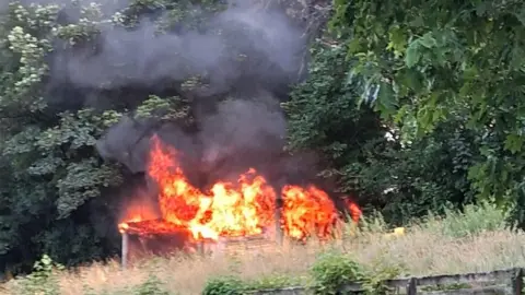 A view of the shelter on fire. Smoke and flames are billowing from the structure.
