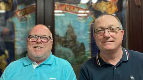 Dayle and Allan Cooke. Both men have short, shaved hair and black-rimmed glasses. They are smiling in the photo.