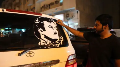 AFP Doha man puts on a car a sticker portraying Qatar's Emir Sheikh Tamim bin Hamad Al-Thani