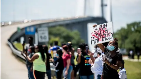 Getty Images Demonstrators watch a parade of passing motorcyclists riding in honor of Ahmaud Arbery