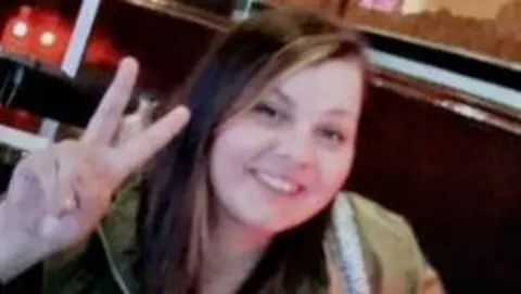 Police Scotland A woman with long brown hair smiles into the camera while giving the peace sign.
