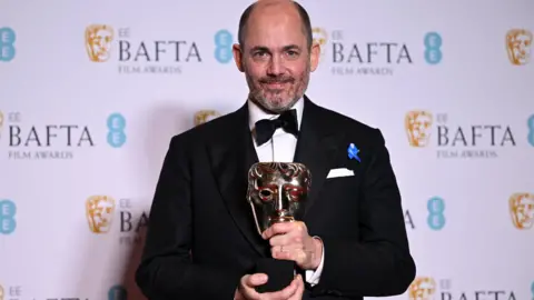 Getty Images German movie director and screenwriter Edward Berger poses with the award for Best director for 'All Quiet on the Western Front' during the BAFTA British Academy Film Awards ceremony at the Royal Festival Hall, Southbank Centre, in London