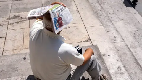 Getty Images A man holds newspaper over his head to shade himself