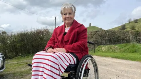 BBC Women smiling sat in a wheelchair in front of Glastonbury Tor