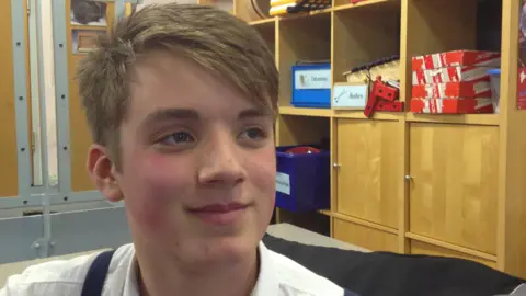 Daniel Spargo-Mabbs Foundation Daniel Spargo-Mabbs smiling with short blonde hair in a white shirt in a classroom. 