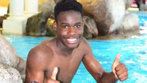 Family handout Shayne Hambakachere. He has short dark hair and is pictured in a swimming pool, looking at the camera, smiling with his thumbs up. 